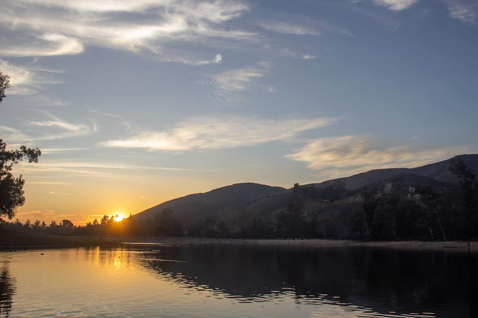 A sunset over a calm lake with mountains in the background.