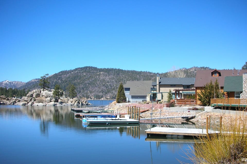 A calm lake with boats docked, a wooden pier, and a mountain in the background.