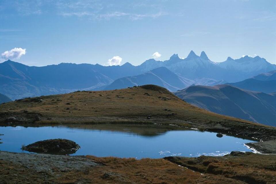 A mountain landscape with a small lake and distant peaks.