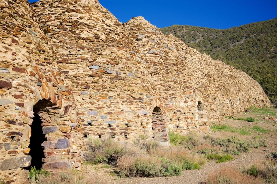 Una estructura de pedra antiga amb obertures en arc, envoltada per herba seca i turons.