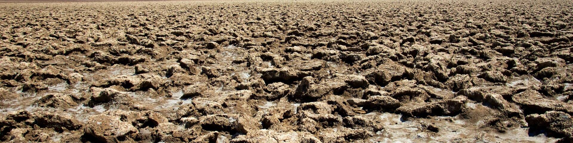 A vast, arid landscape with cracked earth and distant mountains under a clear sky.