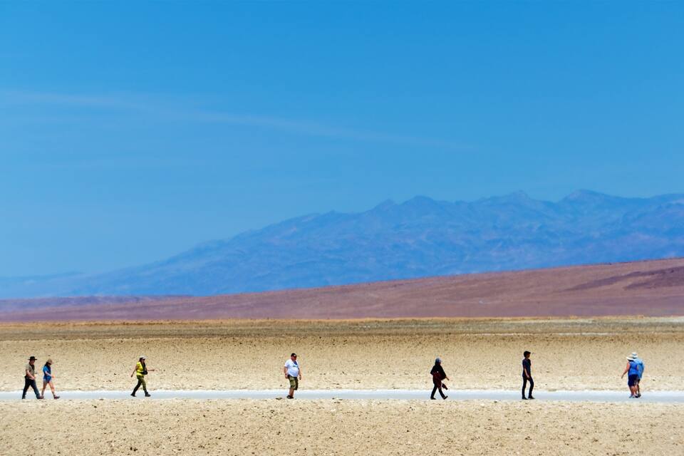 A group of people walking on a salt flat with mountains in the background.