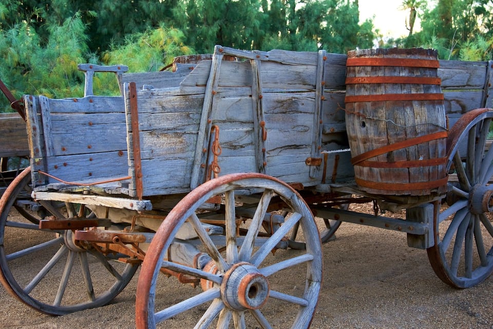 An old wooden cart with large wheels and metal barrels.