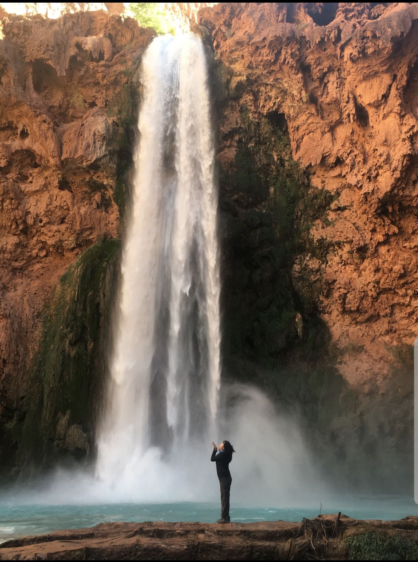 A waterfall cascading down a rocky cliff with a person taking a photo.