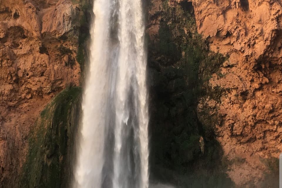 Una cascada se precipita por un acantilado rocoso mientras una persona toma una fotografía.