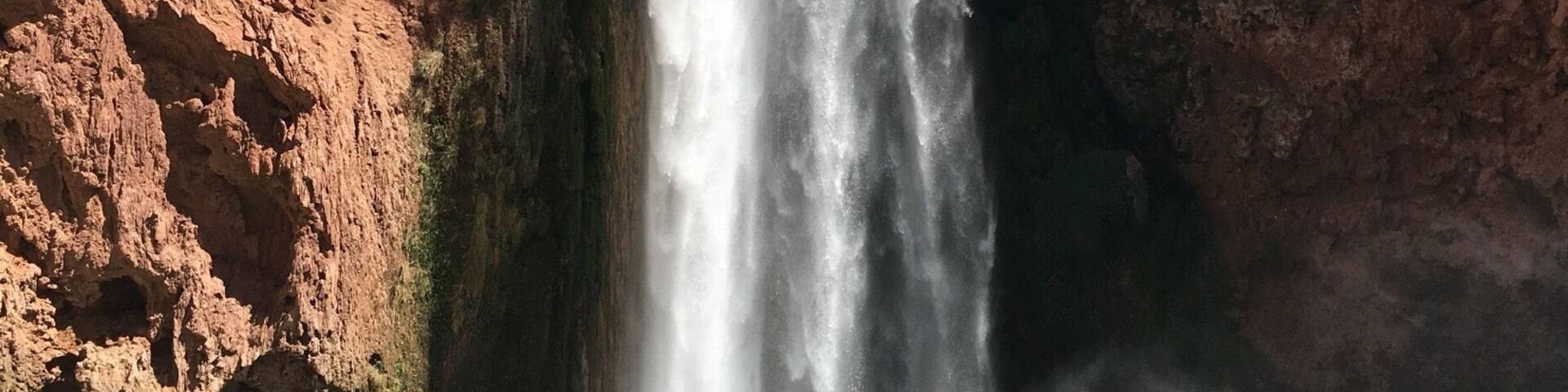 A waterfall cascading down a rocky cliff with a person standing on a rock in the foreground.