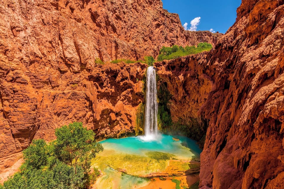 Una cascada en un cañón con paredes de roca roja y una poza turquesa en la base.