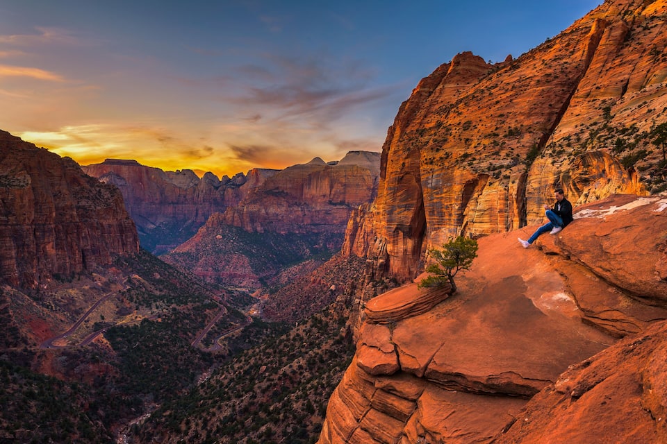 A person sitting on a rock ledge with a canyon in the background.