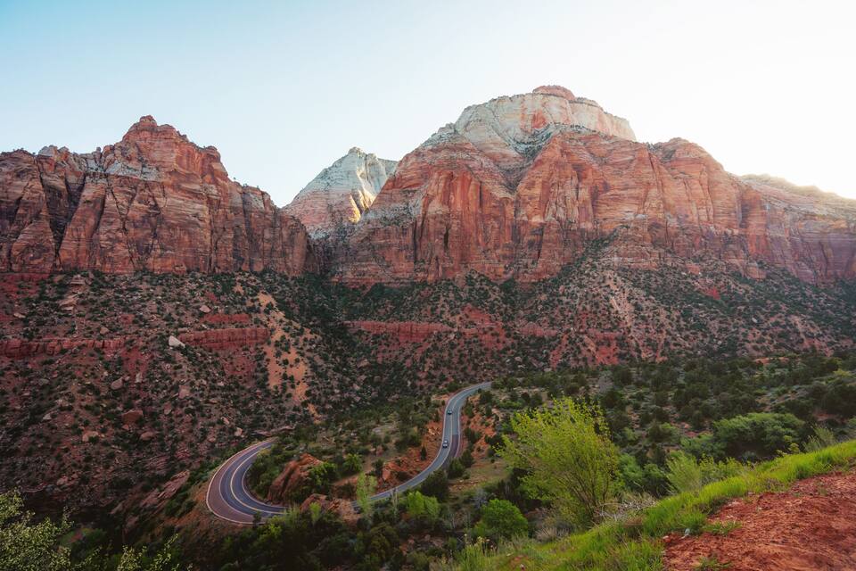 Uma estrada sinuosa serpenteando por uma paisagem montanhosa, com formações rochosas avermelhadas e vegetação escassa.