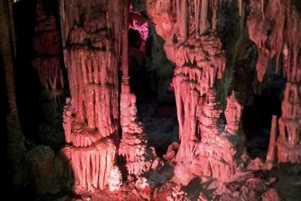 A cave with stalactites and stalagmites illuminated by artificial lighting.