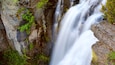 A waterfall cascading over rocky terrain with moss and small plants growing on the rocks.