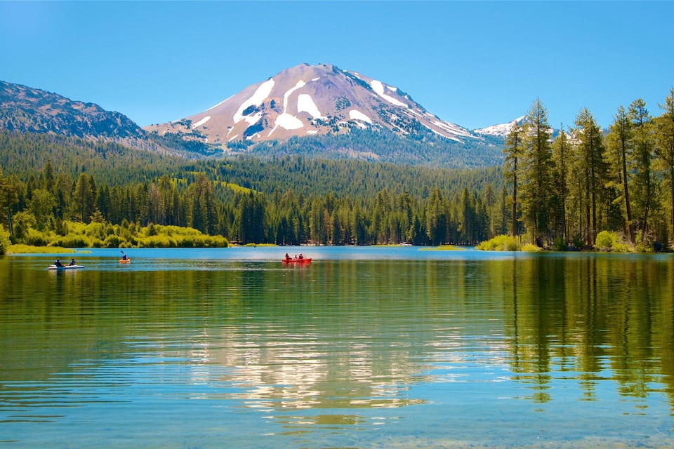 A calm lake with a mountain in the background and dense forest on the sides.