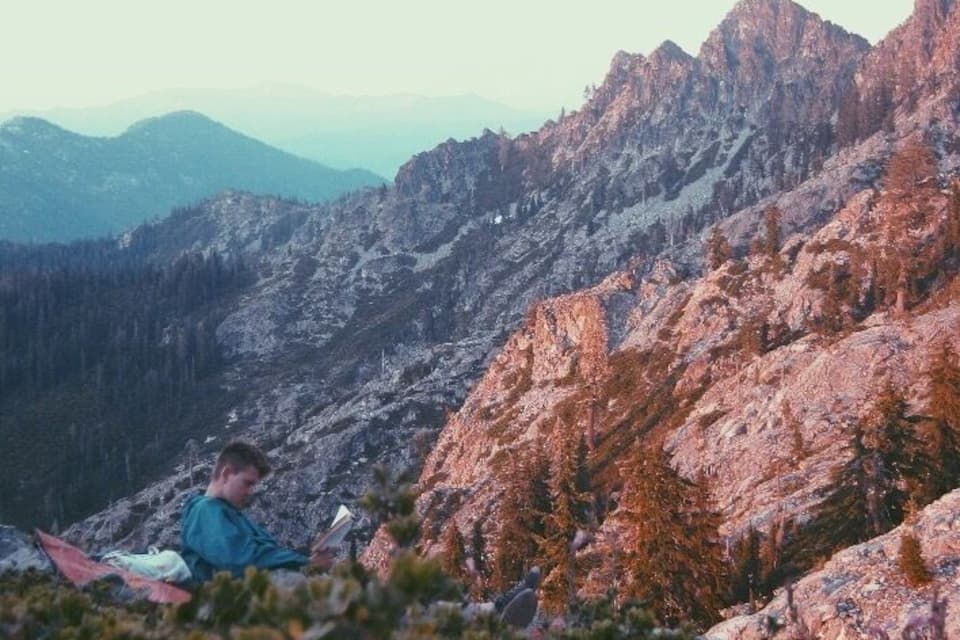 A person sitting on a rock with a mountain range in the background.