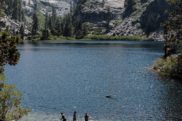 A group of people wading in a lake surrounded by rocky mountains and trees.