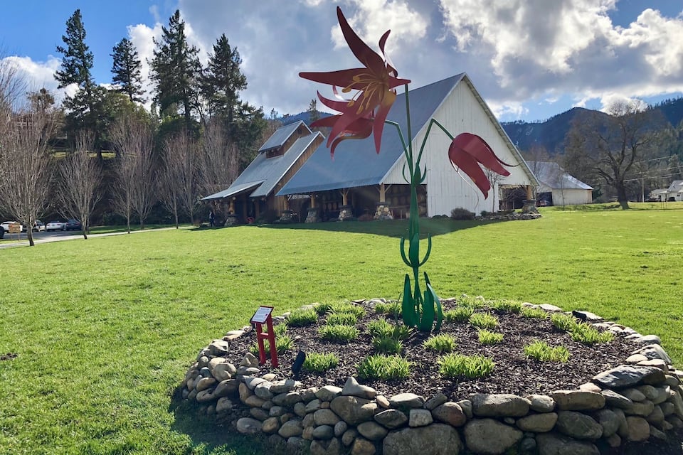 A large red flower sculpture in a grassy field with a white building in the background.