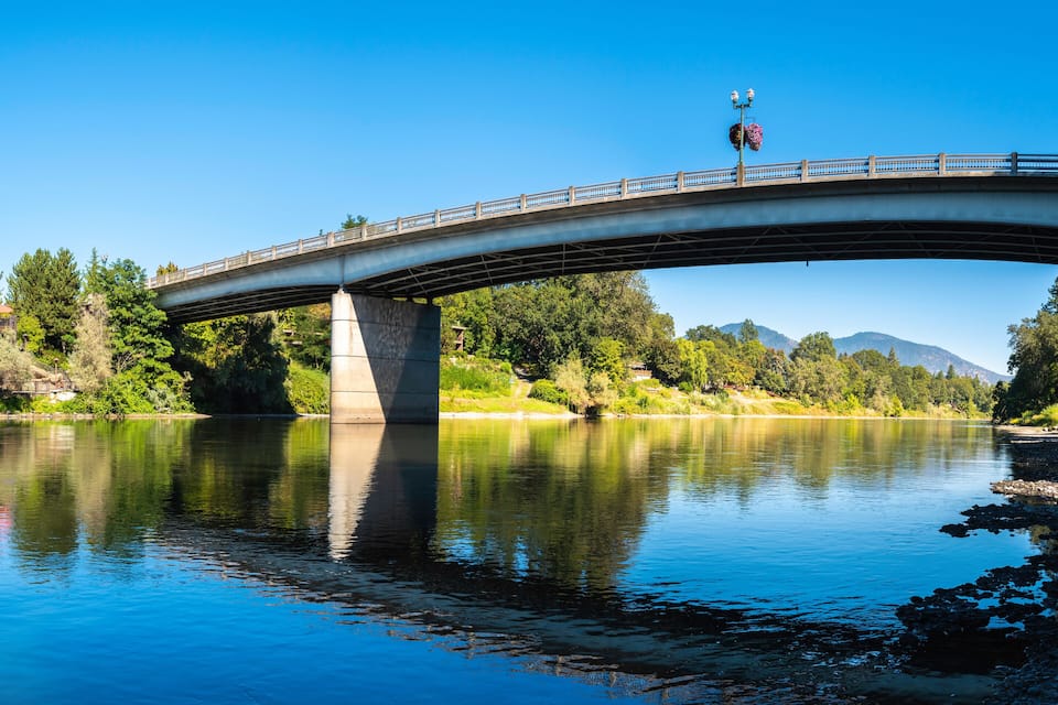 A bridge over a calm river with a building on the left and trees on the right.