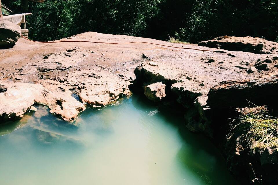 Une source d’eau chaude naturelle, entourée d’un paysage rocheux et d’une forêt dense.