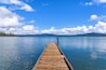 A wooden pier extending into calm water with a clear sky and distant mountains.