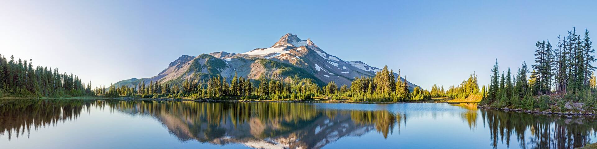 Volcanic mountain in morning light reflected in calm waters of lake.