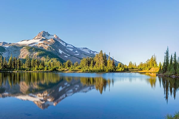 Volcanic mountain in morning light reflected in calm waters of lake.