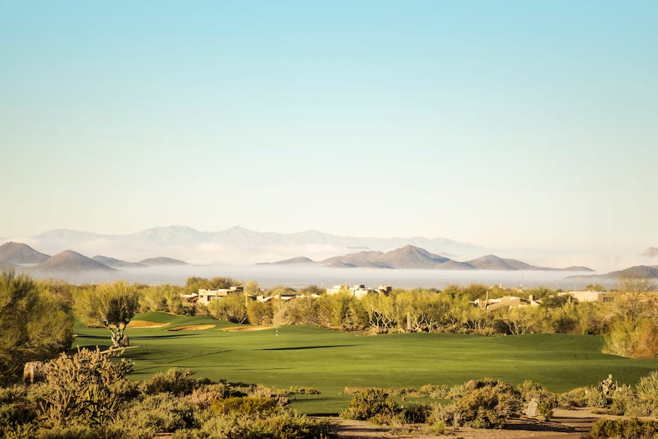 A golf course with a clear view of distant mountains and a town in the background.