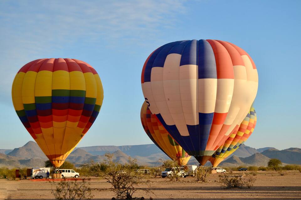 Two colorful hot air balloons in a desert landscape with mountains in the background.