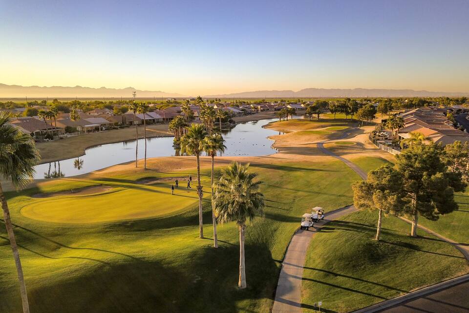 A golf course with a pond, palm trees, and houses in the background.