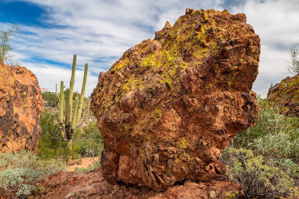A rocky desert landscape with a prominent rock formation, cacti, and sparse vegetation.
