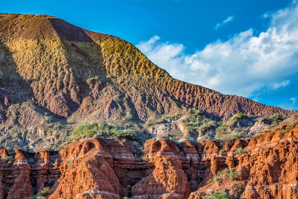 A rugged mountain landscape with layered rock formations and sparse vegetation.