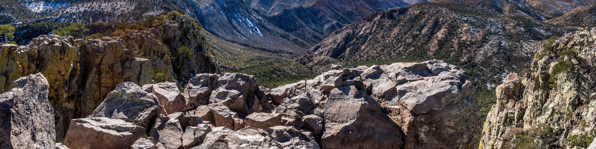 View of a flat rock in the forground situated high above a sloping away valley and snow covered mountain with a skyline in the distance and clouds overhead, Emory Peak, Big Bend National Park, Texas