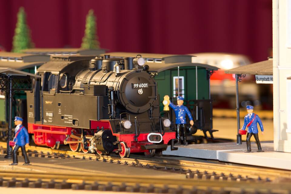 Um comboio modelo com o número 99 6001 na frente, figuras em miniatura e uma plataforma de estação.