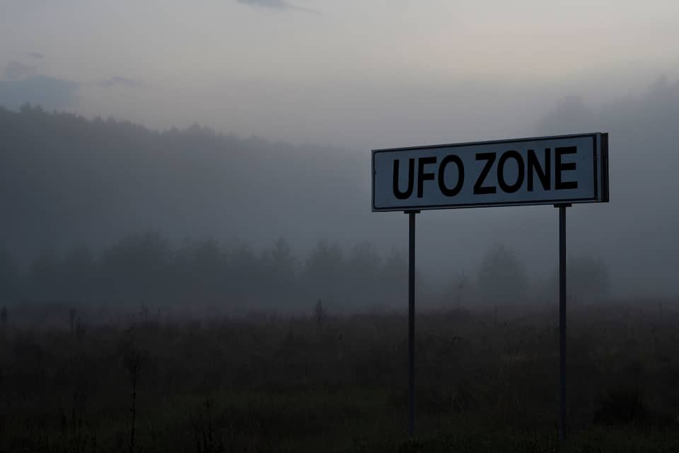 A sign reading "UFO ZONE" in a foggy landscape.
