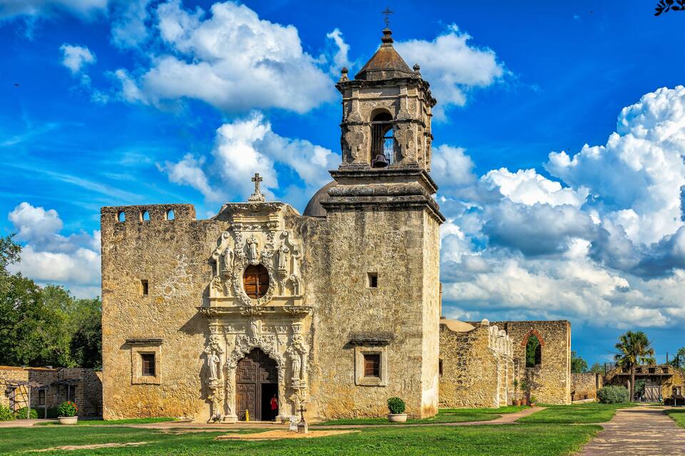 Una iglesia de piedra histórica con un campanario y una entrada ornamentada bajo un cielo azul despejado.