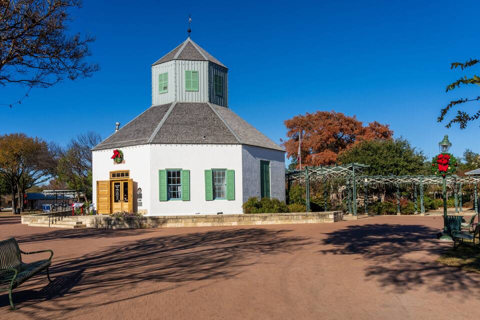 A white building with a green door and shutters, a small tower, and a red flower decoration.