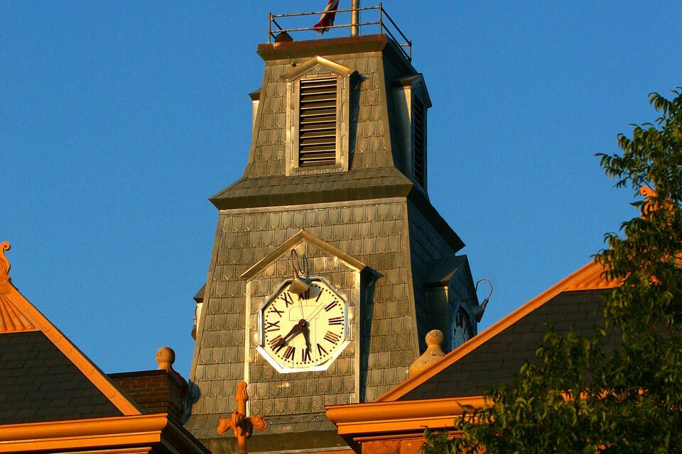 A clock tower with a flag, surrounded by trees and buildings.