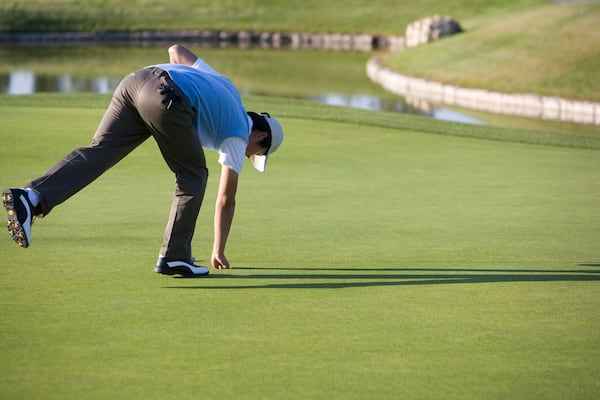 Man picking up golf ball from golf hole