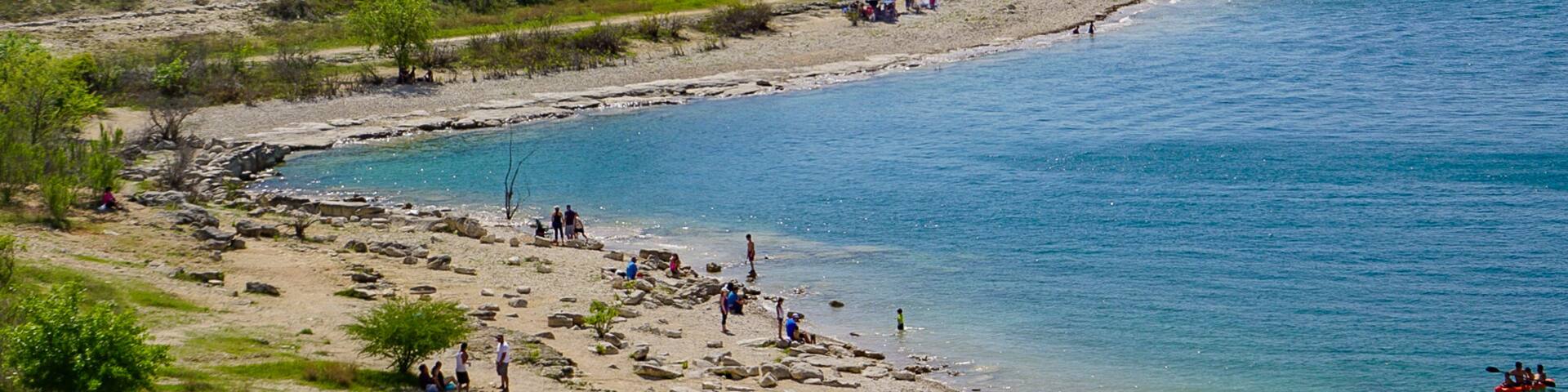 A coastal landscape with a sandy beach, rocky shoreline, and a calm sea.