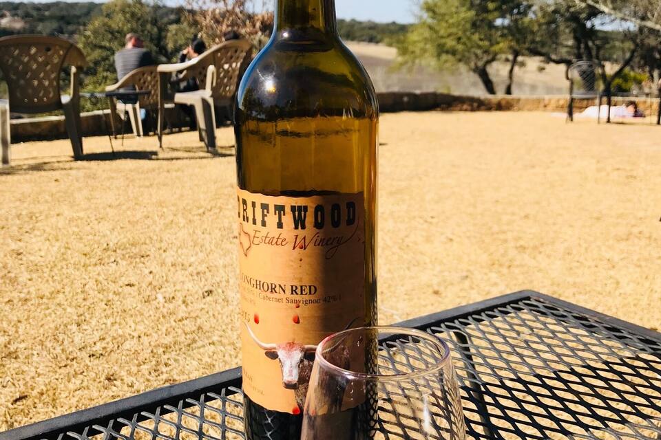 Een fles Longhorn Red wijn en een glas op een metalen tafel buiten.