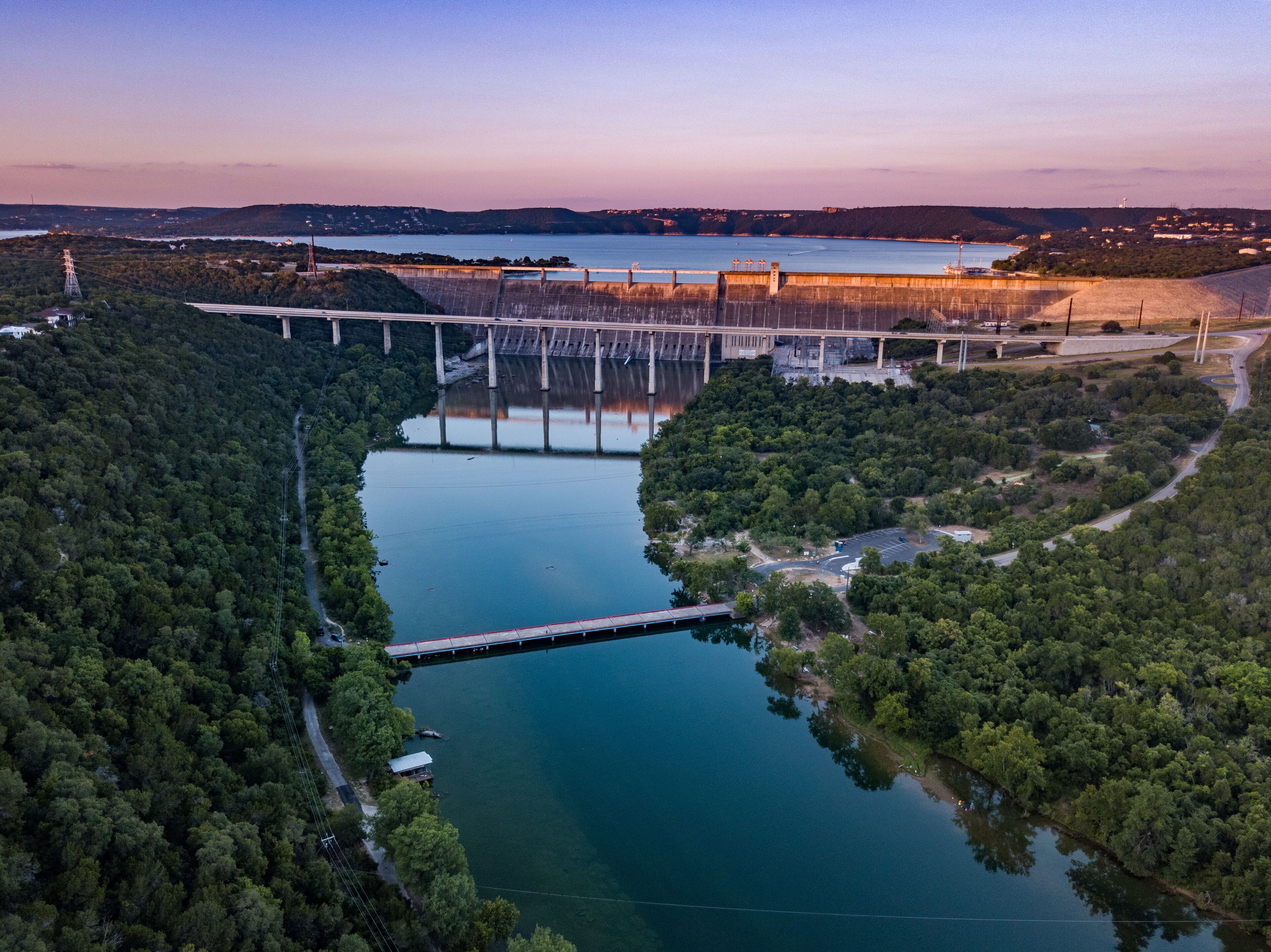 A dam with a bridge, a river, and surrounding forest.