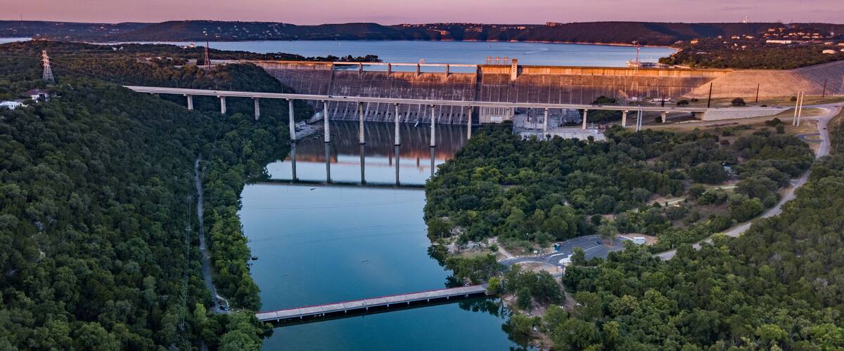 A dam with a bridge, a river, and surrounding forest.