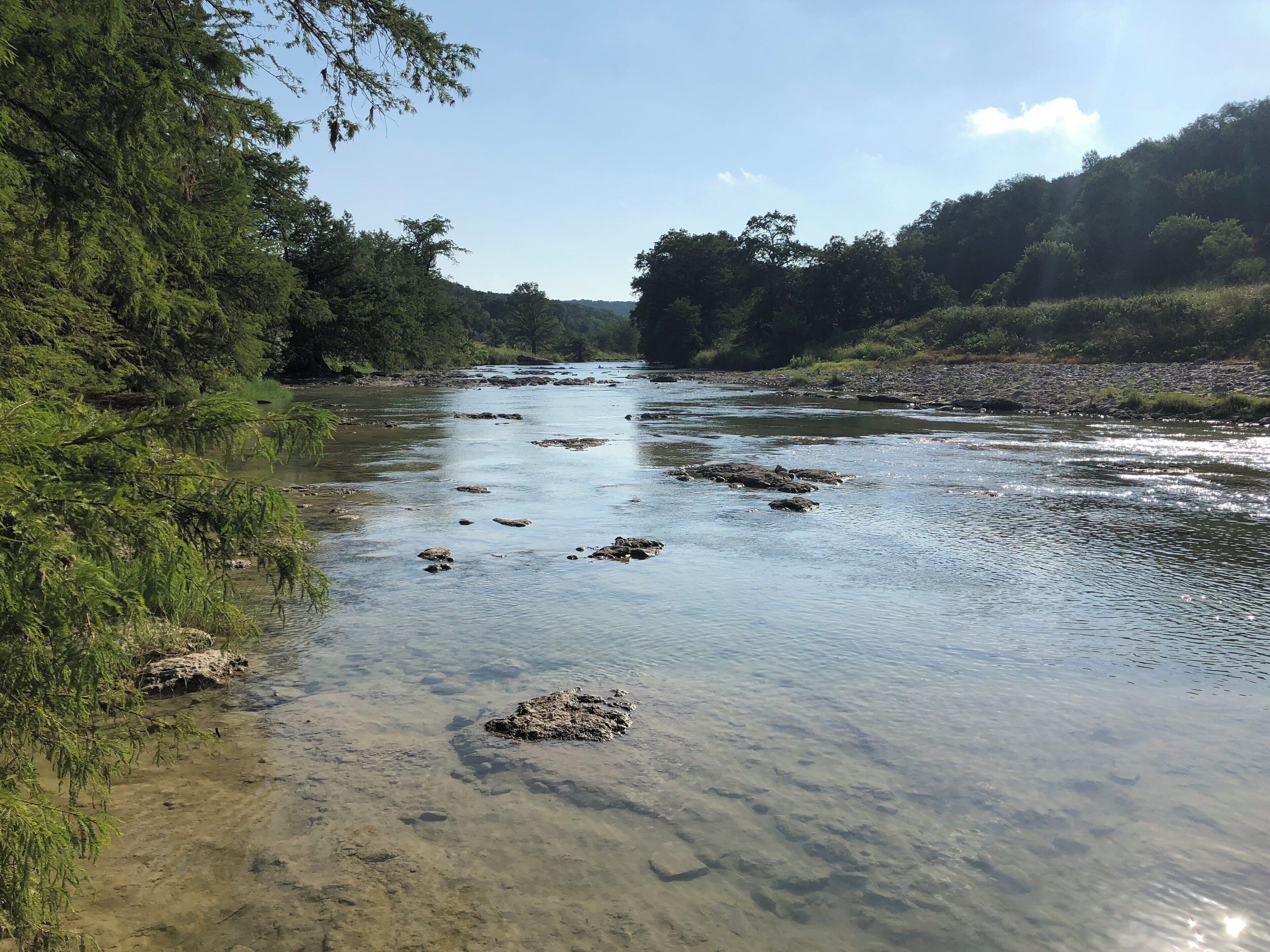 A river with clear water, surrounded by dense greenery and rocky banks.
