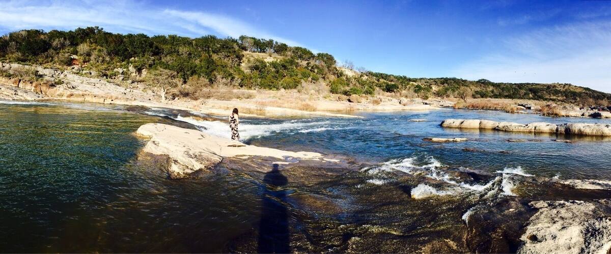 Ein Fluss fließt durch eine felsige Landschaft, eine Person steht auf einem Felsen im Wasser.