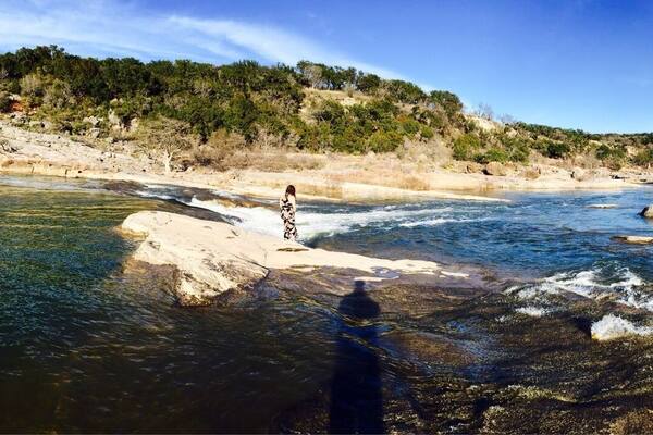 Une rivière qui traverse un paysage rocheux, avec une personne debout sur un rocher dans l’eau.