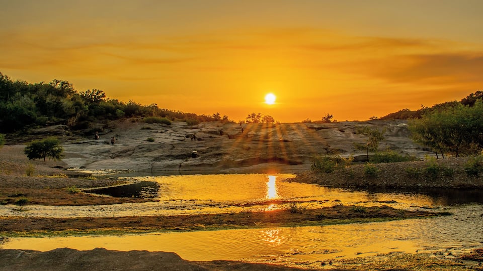 A sunset over a rocky landscape with a reflective water body.