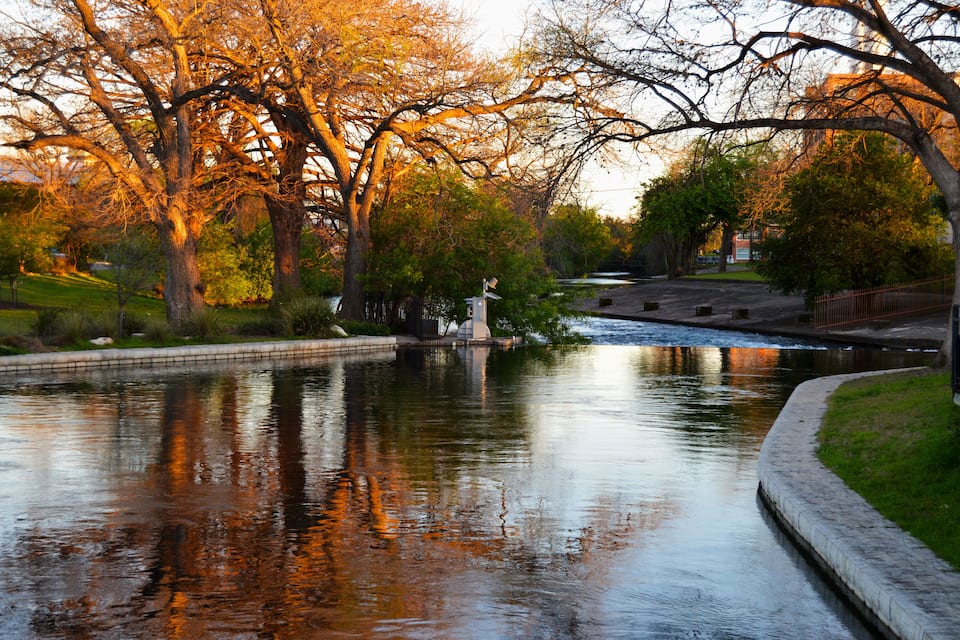 Un riu tranquil amb reflexos d'arbres i un petit pont.