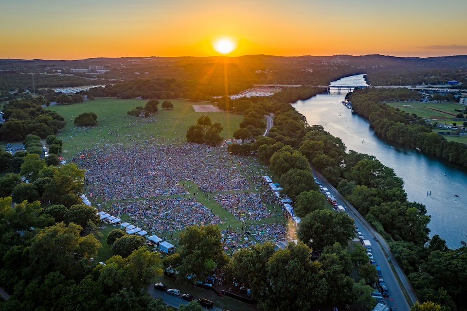 A large outdoor gathering by a river at sunset.