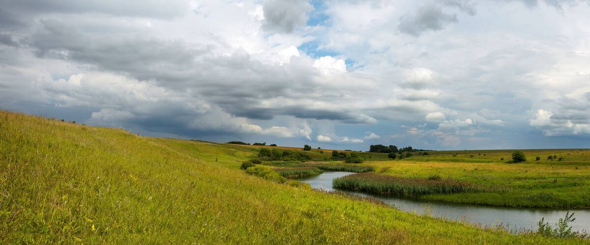 Summer panoramic landscape with dark stormy clouds over the calm river and green meadows.Russian rural landscape.
