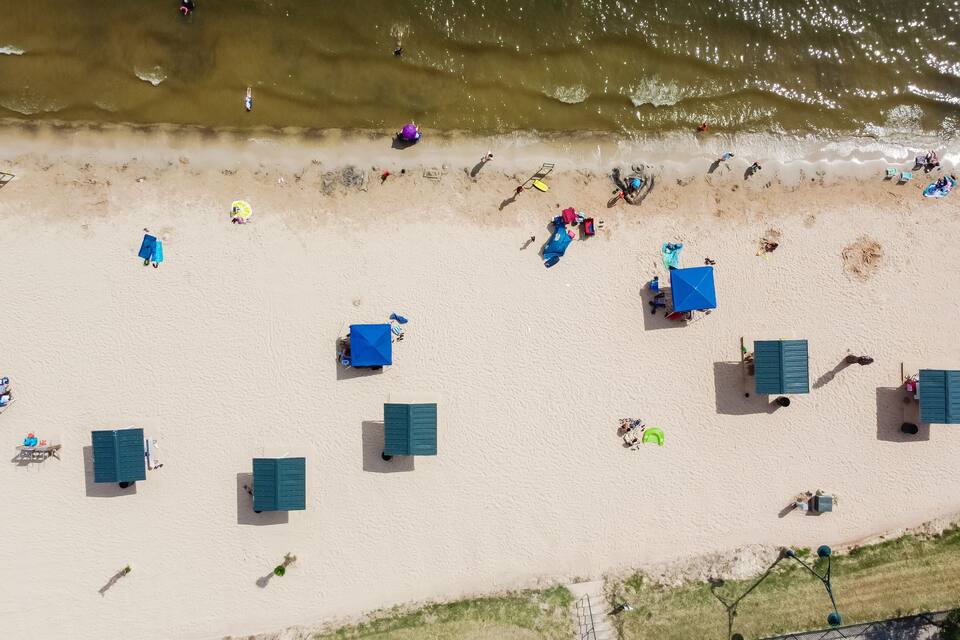 An aerial view of a beach with several blue umbrellas and beach huts.