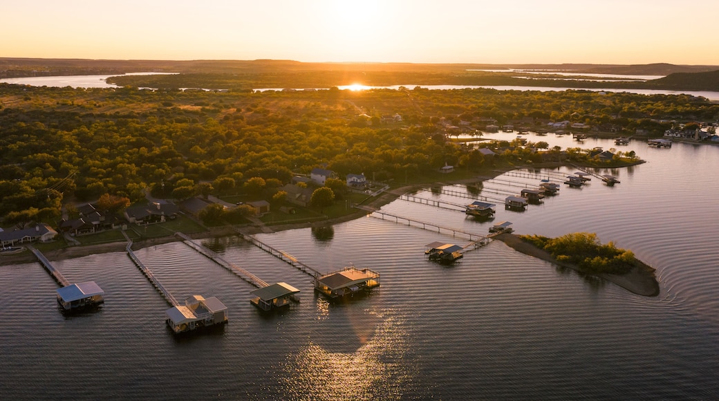 Aerial view of stilt houses stretch into the calm waters as the sun dips below the horizon, casting a warm glow over Possum Kingdom Lake, Possum Kingdom, Texas, United States.