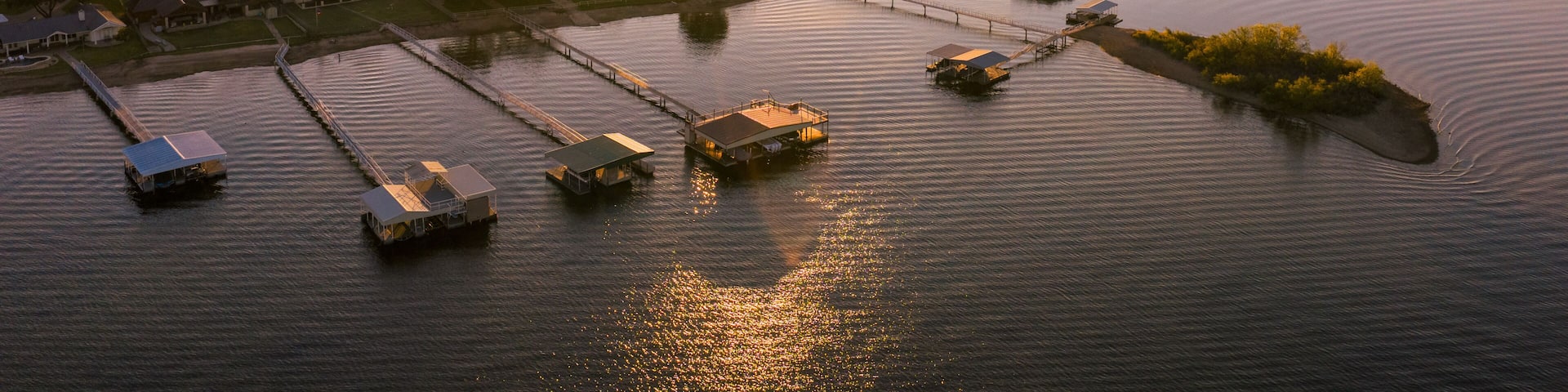 Aerial view of stilt houses stretch into the calm waters as the sun dips below the horizon, casting a warm glow over Possum Kingdom Lake, Possum Kingdom, Texas, United States.
